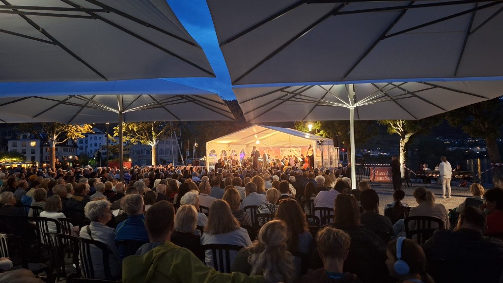 Beleuchtete Open-Air-Bühne am Abend mit Orchester und Publikum am Zürichsee
